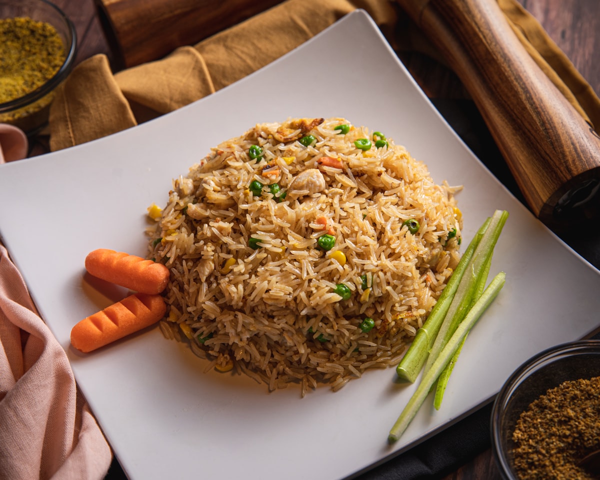 A mound of fried rice with peas and carrots on a white square plate